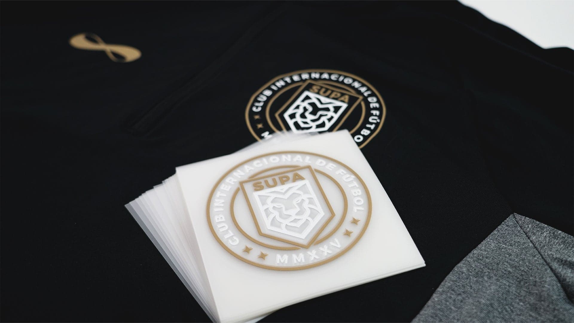 Heat-pressed athletic club badge on black fabric with matching embroidered logo detail